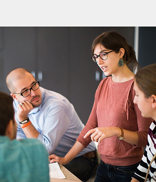 Group of four students talking in a classroom.