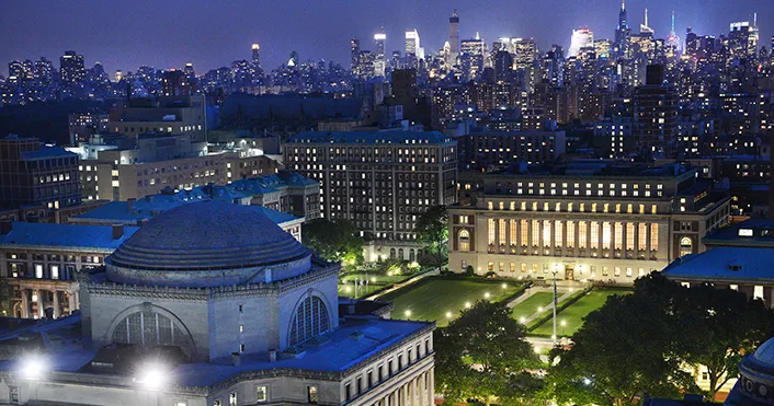 Image of Columbia's Morningside campus at night with New York City in the background.